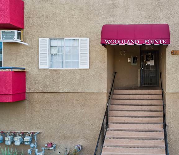 The entrance to a building with a red awning that says Woodland Pointe.