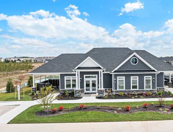 A house with a grey roof and white trim is surrounded by a well-manicured lawn and a clear blue sky.