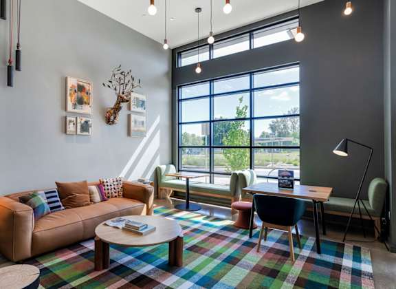 A modern living room with a large window, a sofa, a coffee table, and a colorful rug.