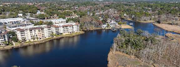 A river flows through a city with apartment buildings on one side and a grassy area on the other at Mandarin Bay Apartments in Jacksonville, FL.