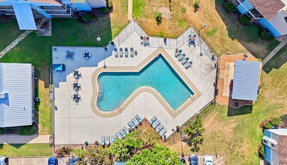 An aerial view of a swimming pool surrounded by a grassy area and a few buildings.
