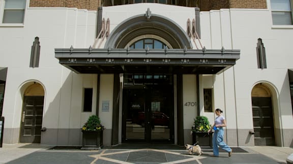 A woman walking her dog in front of a building with the number 4701 on it.