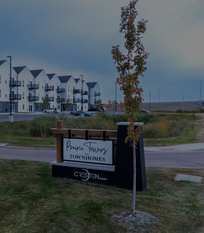 A sign for a place called "Prince Murray Townhomes" is in the foreground of a grassy area with apartment buildings in the background.