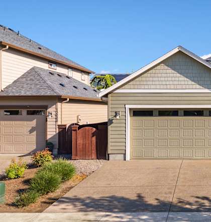 A house with a grey garage door is in front of a green lawn.