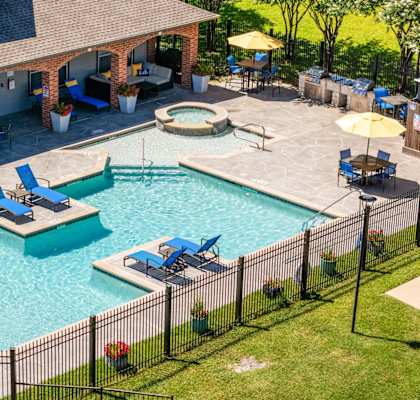 A pool surrounded by a black fence with blue lounge chairs and yellow umbrellas. at Clear Creek Meadows Apartments, Apartments, Copperas Cove, TX
