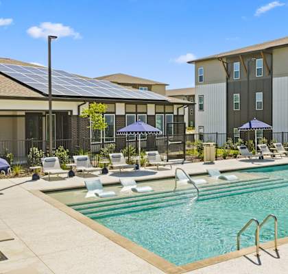 A swimming pool with a slide and sun loungers in front of a building.
