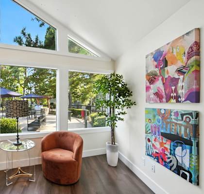 Two brown chairs are placed in front of a wall with a painting and a potted plant.