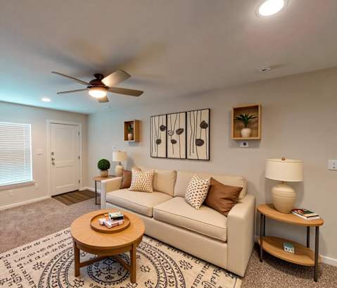 A living room with a beige couch, a coffee table, and a ceiling fan.