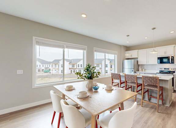 A dining room with a table set for four and a kitchen area in the background.