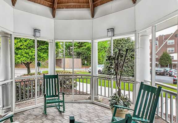 A white gazebo with a wooden roof and a white railing with a green chair and a potted plant.