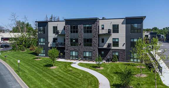 an apartment building with green grass and a sidewalk