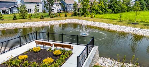 A pond with a bench and a fence in the foreground with houses in the background.