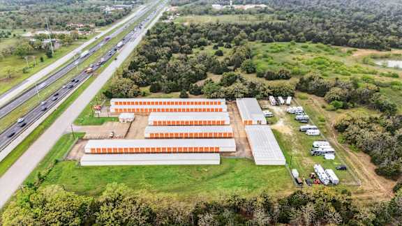 A large orange building is surrounded by greenery and is located next to a highway.