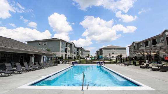 A swimming pool in front of a building with lounge chairs around it.