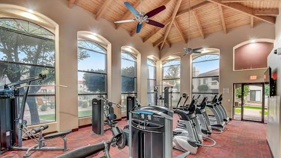 A gym with a variety of equipment including treadmills, weights, and a rowing machine. at San Montego Apartments, Mesa, Arizona