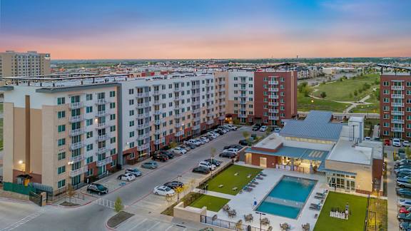A view of a residential area with apartment buildings, a swimming pool, and a parking lot.