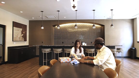 Two people sitting at a table in a room with a large painting on the wall.