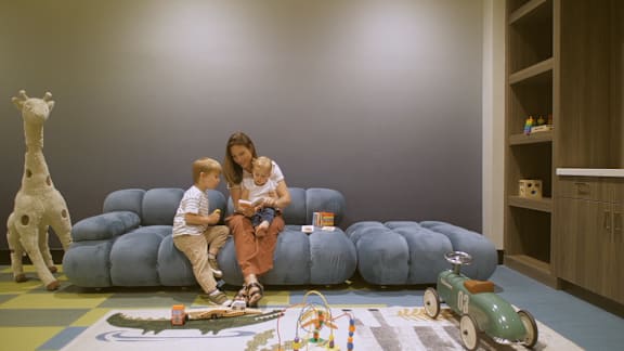 A woman and two children are sitting on a blue couch in a room with a wooden floor and a grey wall.