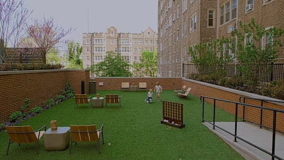 A man is standing in a courtyard with a green lawn and a brick wall.