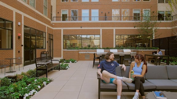 Two people sitting on a bench in a courtyard.
