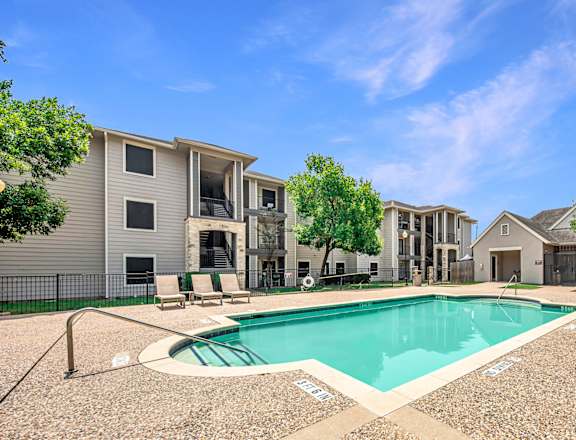 A swimming pool surrounded by a gravel area and apartment buildings.
