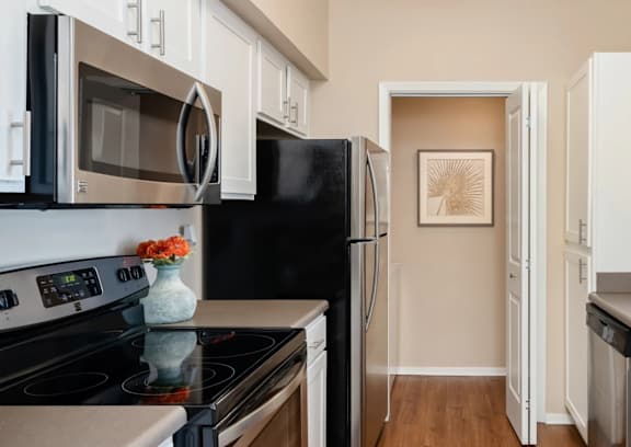 A kitchen with a black refrigerator and a stove with a vase of flowers on it.