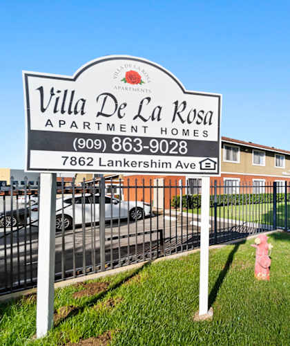 A sign for Villa De La Rosa Apartment Homes stands in front of a building.