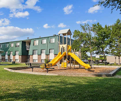 a playground in front of a green building with a yellow swing set