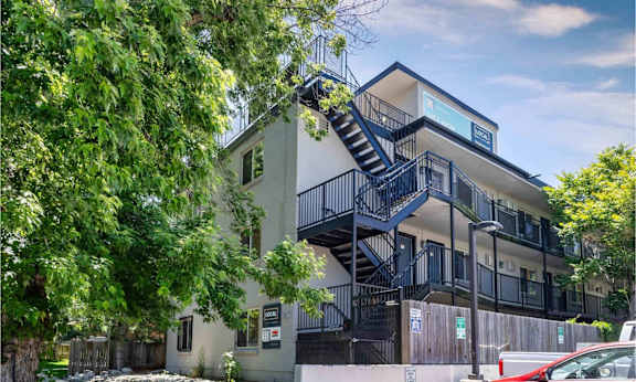 Contemporary apartment building with black metal staircases, balconies, and mature trees surrounding the property at 1443 Elizabeth in Denver, CO