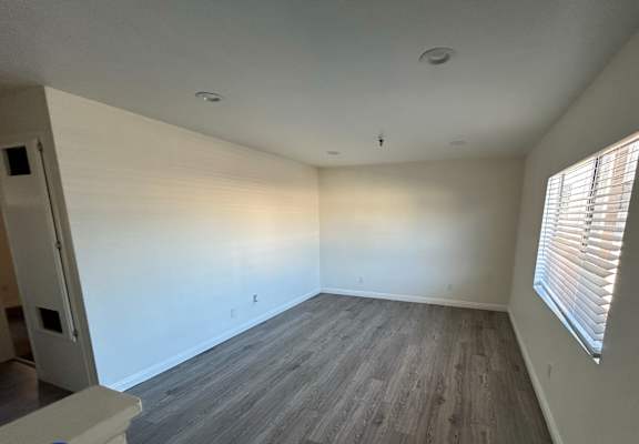 A room with wooden flooring and a window with blinds.