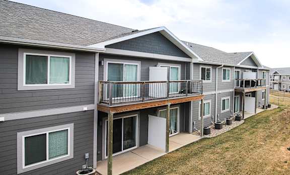 A grey building with a balcony and a green lawn in front.