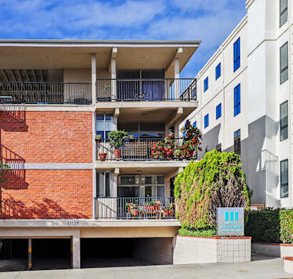 A red brick building with a balcony and a blue sign in front.
