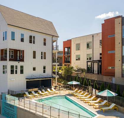 A pool surrounded by chairs and umbrellas is in front of a building.