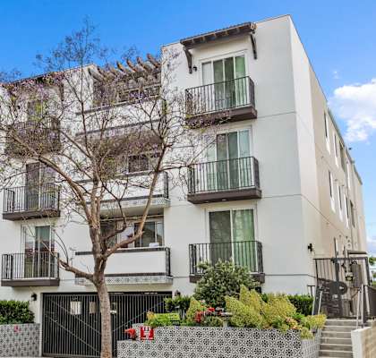 a white apartment building with balconies and a tree in front