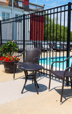 A black metal fence surrounds a pool area with chairs and a table at The Argonne Apartments, Washington, DC, 20009