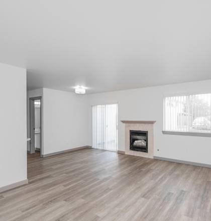 A spacious room with a fireplace and wooden flooring.