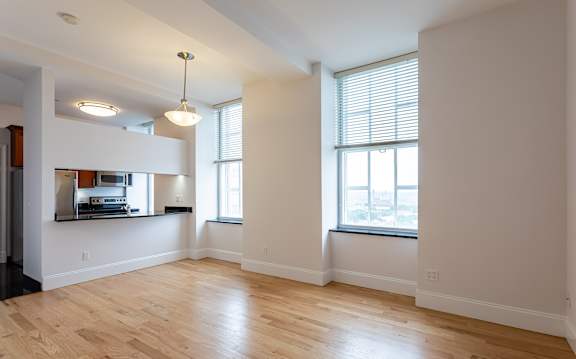 A large empty room with wooden floors and a window with blinds.