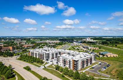 A large, modern building complex is surrounded by a green landscape and a roadway.