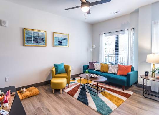 Butchertown Apartments - Martin on Main - Living Room with Colorful Area Rug, Couch, Chair, Coffee Table, Ceiling Fan, and Window.