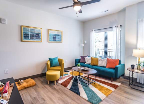 Butchertown Apartments - Martin on Main - Living Room with Colorful Area Rug, Couch, Chair, Coffee Table, Ceiling Fan, and Window.