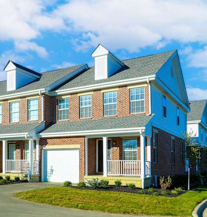 A red car is parked in front of a two-story house.
