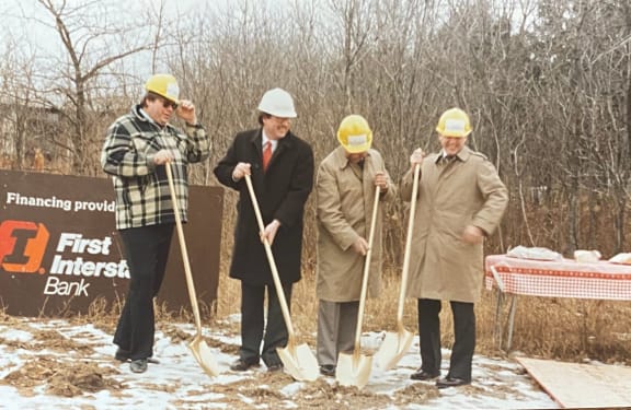 four men in hard hats holding shovels in the snow