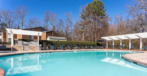 A large swimming pool with a white pergola and trees in the background.