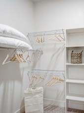 a closet with white curtains and white shelves and a bed with white pillows