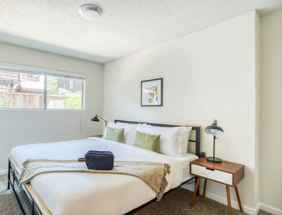 A bedroom with a bed, nightstand, and window.