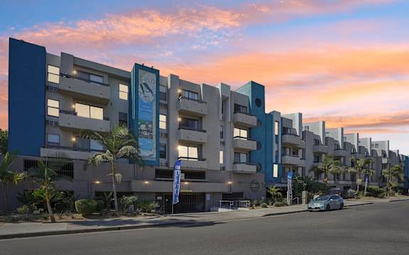 A modern apartment complex with a blue car parked in front.