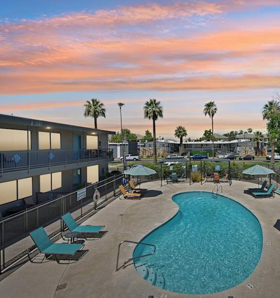 A pool surrounded by chairs and umbrellas in a sunny courtyard.
