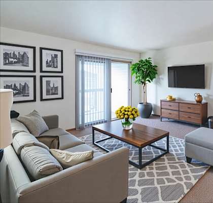 A living room with a grey couch, a coffee table, a plant, a TV, and a brown door.