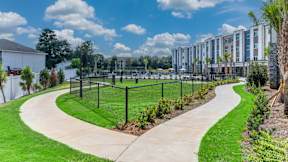 A pathway with a green grassy area on the left and a fence on the right.