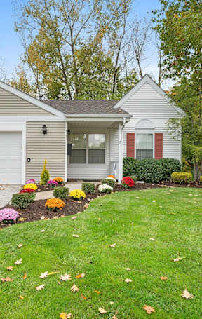 A house with a grey roof and white garage doors is surrounded by a garden with colorful flowers.